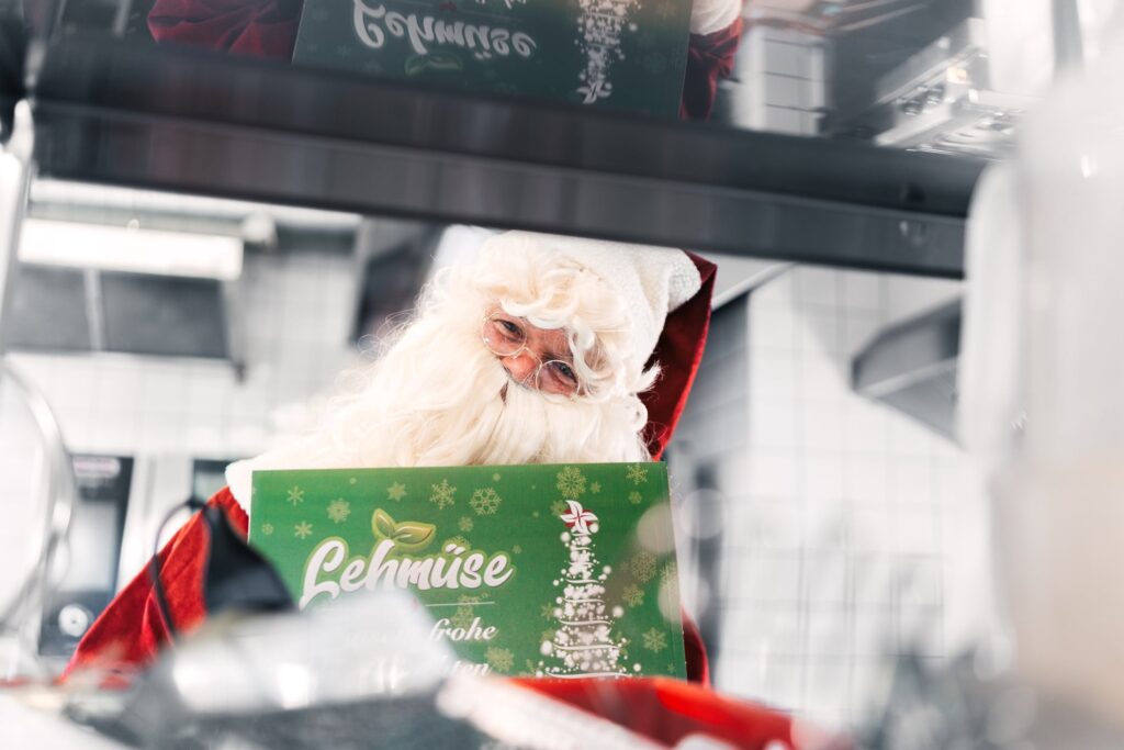 Lehmi im Weihnachtsmannkostüm schaut in die Kamera und hält einen Karton für die Weihnachtsbox von Lehmüse in der Hand
